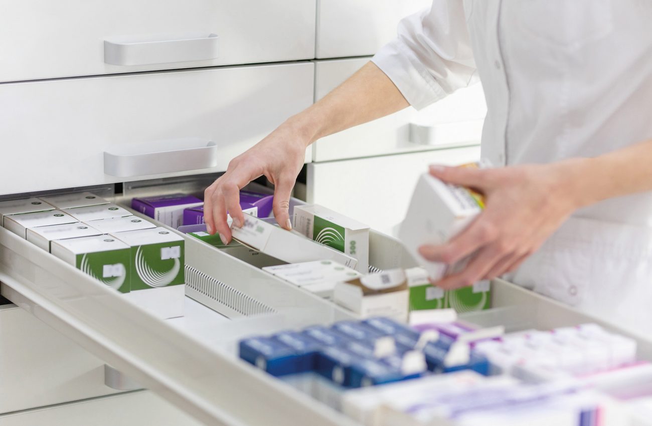 Pharmacist holding medicine box and capsule pack in pharmacy drugstore.